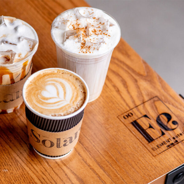 Coffee drinks from Solare Café at Element Eatery food hall, featuring a hot latte with latte art and two iced drinks topped with whipped cream and caramel drizzle