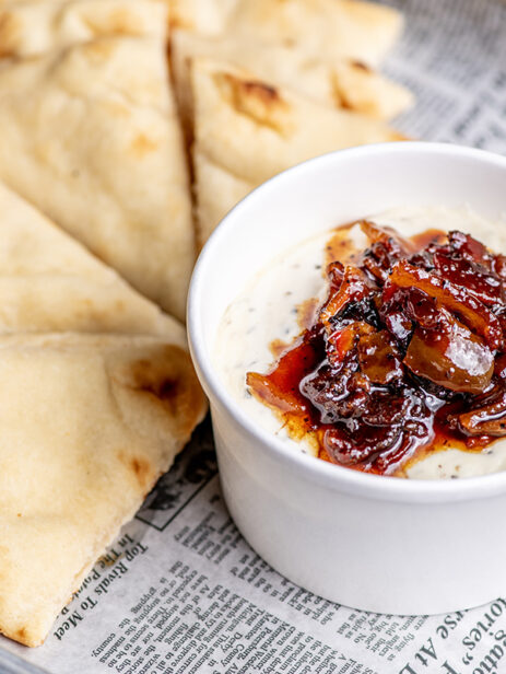 Goat cheese dip topped with bacon onion jam, served with warm naan from London Street Eats by The Pub at Element Eatery food hall on a newspaper-lined tray