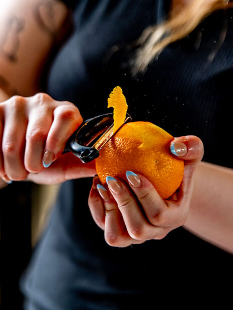 Bartender peeling an orange garnish for a cocktail at The Garden bar in Element Eatery food hall